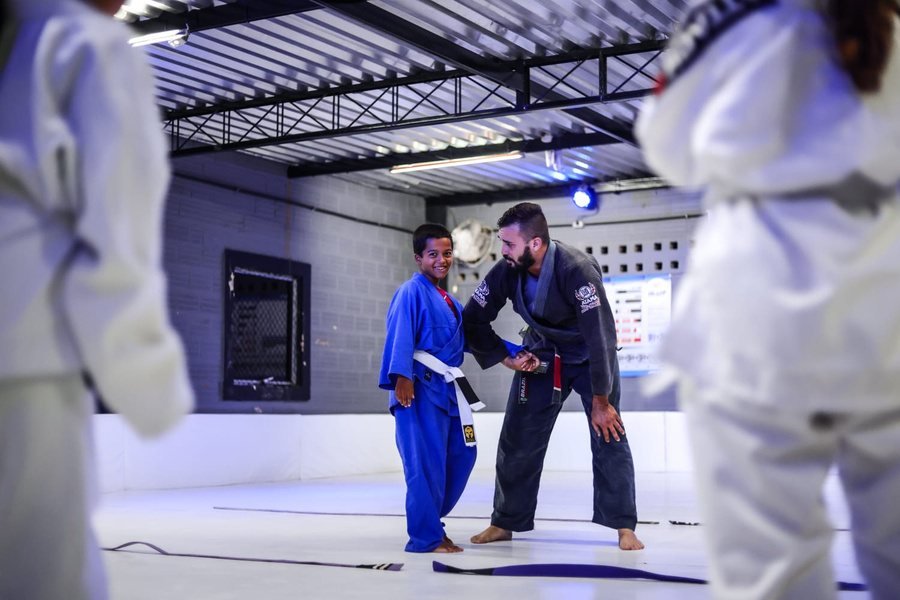 Professor Matheus Coimbra corrige a posição de um aluno durante aula de Jiu-Jitsu Kids